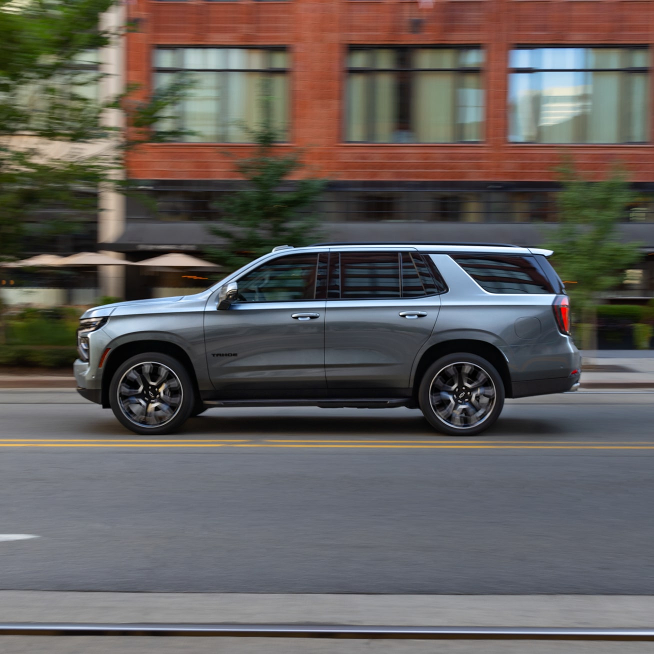 Side View of the 2025 Chevrolet Tahoe SUV Driving on a Road Lined with Businesses